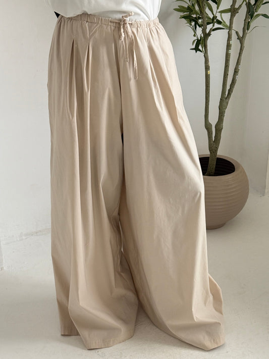 Light beige Amenaa wide leg pants displayed on a hanger, featuring a relaxed fit and flowing fabric for casual or stylish wear.