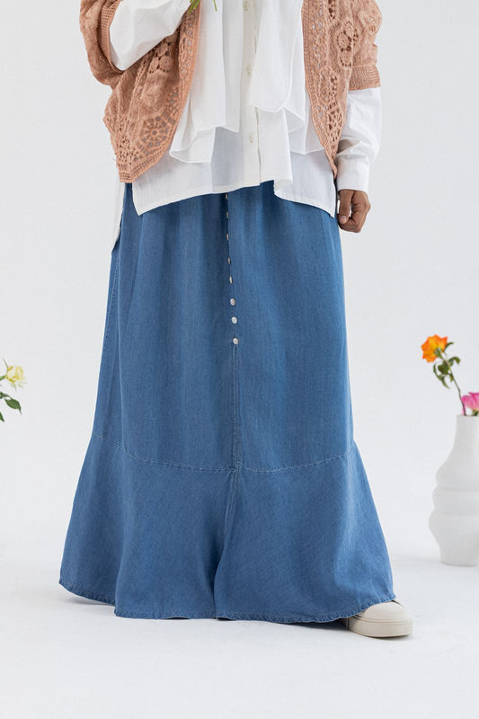 Light denim skirt by Amenaa, showing the high-waisted design with front button closure and rolled hem detail.