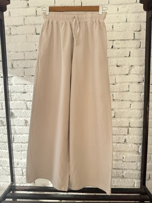 Beige Amenaa gabardine wide-leg pants displayed on a hanger, showcasing their relaxed fit and smooth fabric.