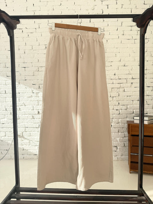 Beige Amenaa gabardine wide-leg pants displayed on a hanger, showcasing relaxed fit and smooth fabric texture.