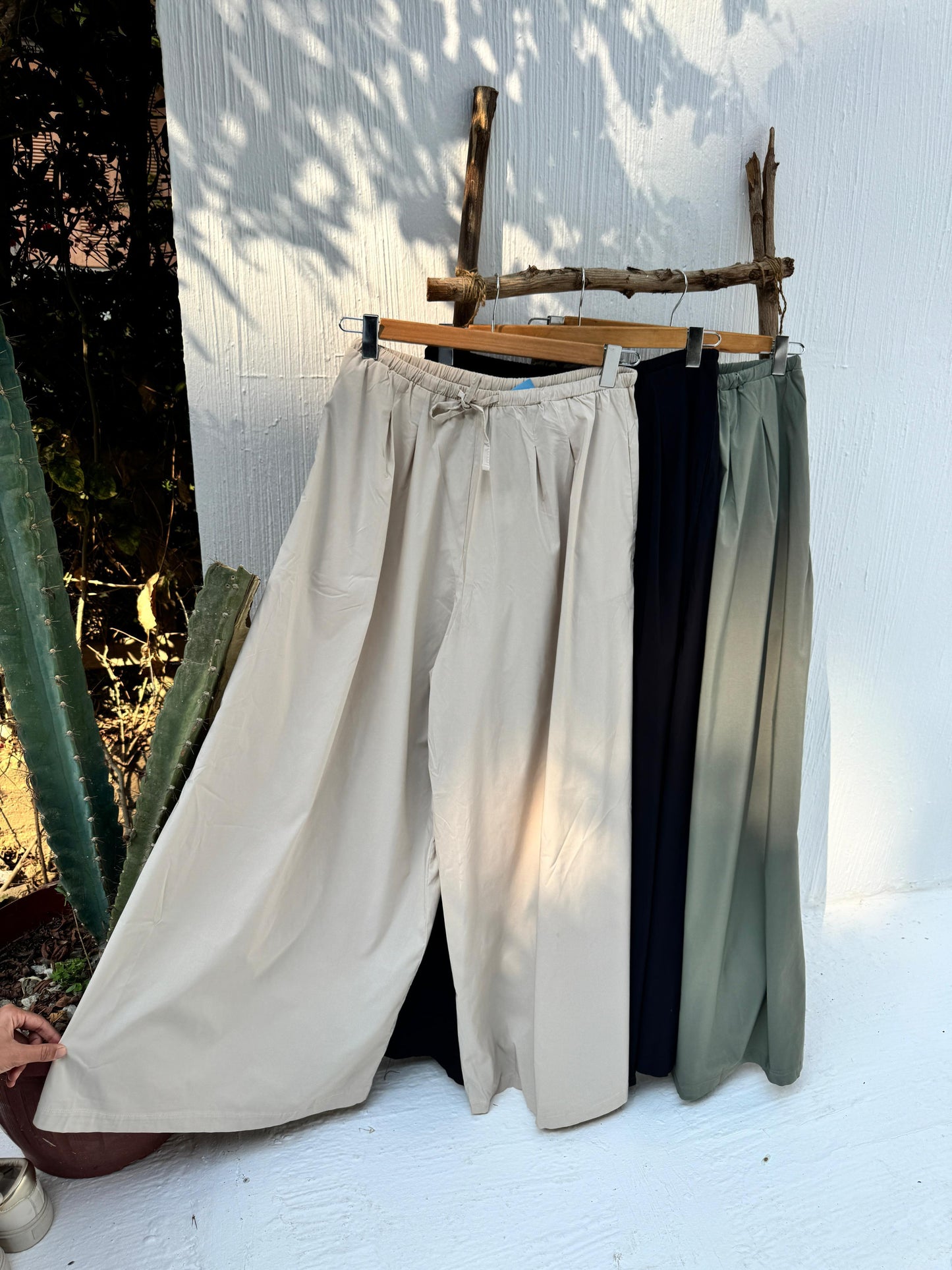 Amenaa wide leg pants in beige, featuring a relaxed fit and high waist, displayed on a wooden background.